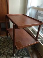 Front perspective of teak tea cart showing two trays and casters