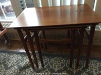 Front view of three nested teak tables showing tapering legs