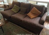 Front view of three seater sofa with multi-colored upholstery and three cushions in green, brown, and orange patterned fabrics.
