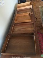 Five wood trays arranged on a table showing size and shape differences, the two butler trays with handles and three office trays with raised edges.
