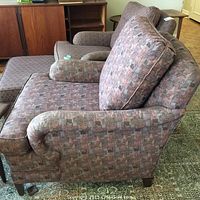 Side view of the multi-coloured patterned upholstered chair with cushioned armrests and wooden legs.