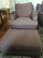 View of the upholstered armchair and matching ottoman from an angle showing the seating and ottoman top surfaces along with adjacent room elements.