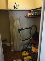 Photo of laundry room corner showing yellow Panasonic vacuum cleaner, ironing board, folding drying rack, shoe rack, and hangers on closet rod.