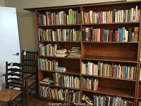 Full view of the large wooden bookcase filled with various books and two chairs nearby.
