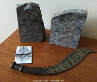 View showing both stone bookends, decorative metal dagger, and painted metal plaque arranged on a wooden surface.