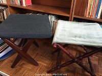 Two folding stools side by side, one with dark fabric seat and teak frame, the other with light green velour-like fabric seat and mahogany frame