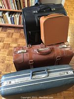 Four pieces of luggage stacked showing overall condition and colors, including Samsonite, leather case, black canvas wheeled suitcase, and small tan case.