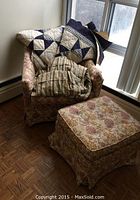 Upholstered living room chair with floral pattern, quilt draped over the back, and ottoman in front of a window