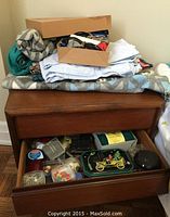 Full view of the teak night table showing top cloths/fabrics and the two drawers, with the bottom drawer open revealing sewing supplies arranged inside.
