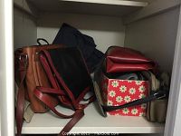 Purses on a shelf including a brown leather handbag, black purse with maroon trim, and a smaller dark brown leather purse partially visible in a floral box.