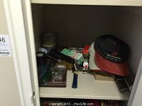 Shelf contents showing mixed lot of hand tools, hardware, lightbulbs, duct tape rolls, and several baseball caps.