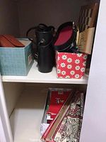 Shelf with black leather case holding Steiner binoculars, wood chess board, and Christmas decor boxes.