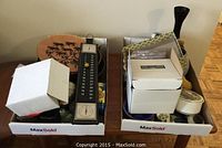 Two boxes filled with assorted small decor items including pottery, trinket dishes, candles, candle holders, decorative plates and a thermometer