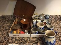 Front view showing the assortment of pottery dishes, pitcher, wooden bowls, copper kettle, and additional kitchen items arranged in two boxes.