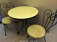 Round yellow laminate top kitchen table with black wrought iron base and two matching wrought iron chairs with yellow vinyl seats.