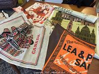 Photo showing five tea towels or wall hangings of various themes including painted silk and printed fabric laid out on a table.