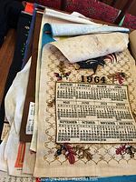 Photo of a cloth tea towel calendar from 1964 featuring a floral border with visible discoloration and age marks.