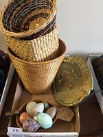 Alabaster eggs in wooden bowl beside woven wicker baskets and brass plaque.