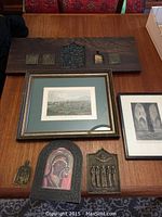 Overview of all items including framed prints, wooden plaque with brass pieces, and individual brass plaques on table.