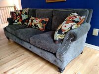 Gray fabric sofa with three decorative floral pillows against a blue wall, showing the right side and front view.