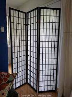 Full view of the three-panel room screen standing in a room with black framed grid and white translucent insert panels.