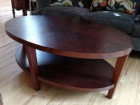 Oval wooden coffee table shown from side angle, highlighting shape and shelf below.