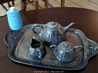 Full view of silverplate tea service on tray showing teapot, sugar bowl, and creamer. Tray has decorative handles.