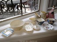 Various Belleek, Wedgwood, and Chintz porcelain pieces displayed on a window ledge under natural light.
