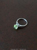 Photo of 14K white gold ladies ring with yellowish green stone on a brown textured surface, showing top and side views and band marking.