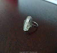 White gold filigree ladies ring with three diamonds on the top, positioned on a dark surface.