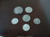 Six silver coins including two 1976 Bicentennial Kennedy half dollars, three Washington quarters from 1946, 1954, and 1964, and one 1878 silver dollar visible on a dark brown surface.