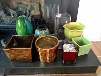 Photo of various vases and pots arranged on a dark table surface with a fireplace background.
