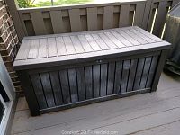 Full front and top view of large weather-resistant plastic outdoor deck box with hinged lid and wood texture.