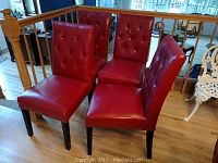 Four red leather dining chairs arranged together on a wooden floor by a stair railing, showing full side and front views.