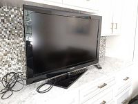 Samsung 40 Inch Television placed on a white countertop, powered-off screen, power cords visible coiled beside the unit.