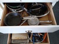 Drawer with assorted pots and pans, including small frying pans, saucepans, and glass lids