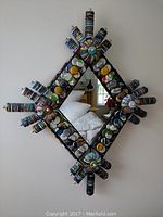 Photo of a kitschy diamond-shaped mirror with multiple colorful bottle caps woven around the frame.