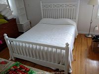 Wide view of assembled white wooden bed frame with bedding in room showing headboard, footboard, and bedding.