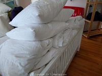 Stack of white queen size comforters and pillows on a bed frame.