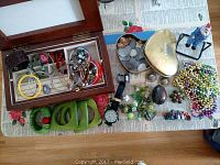 Wide view showing all jewelry pieces including bangle bracelets, pins, watch, beaded necklaces, and decorative items arranged on newspaper-covered table.