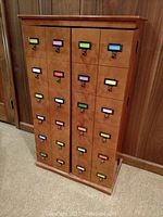 Wooden CD cabinet closed, showing two doors with multiple small drawers fitted with colorful label holders and metal pulls in a grid arrangement.
