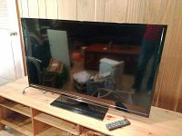 Front view of television on wooden stand with remote control on the shelf