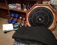 Photo showing the collection of items including hand weights, dumbbells, Crokinole board, sleeping bag, medicine ball, trophies, toy cars, comforter, and white binder on carpet and wooden shelf in background
