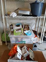 Photo of plastic containers and cardboard boxes containing various light bulbs and electrical accessories on and near metal shelving unit.