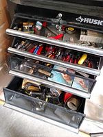 Husky tool chest open with multiple drawers showing various hand tools including screwdrivers, pliers, and measuring tape.