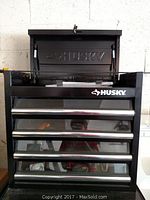 Front view of the black Husky metal toolbox with the top lid open showing embossed Husky branding.