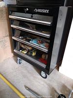 Full view of the black Husky toolbox showing the stacked drawers and wheels on the floor.