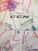 Close-up image showing CCM brand logo, the number 15, and autograph by Sam Field on the white hockey sock with colorful artwork.