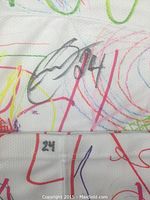 Close-up photo showing the player's autograph signed with black marker and the number 24 on the sock, along with colorful drawings and scribbles in the background.