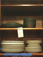 Four dark green ceramic bowls stacked next to four matching dark green plates stacked on a shelf